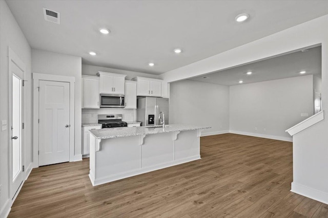 kitchen with dark wood-type flooring, white cabinetry, appliances with stainless steel finishes, an island with sink, and light stone countertops