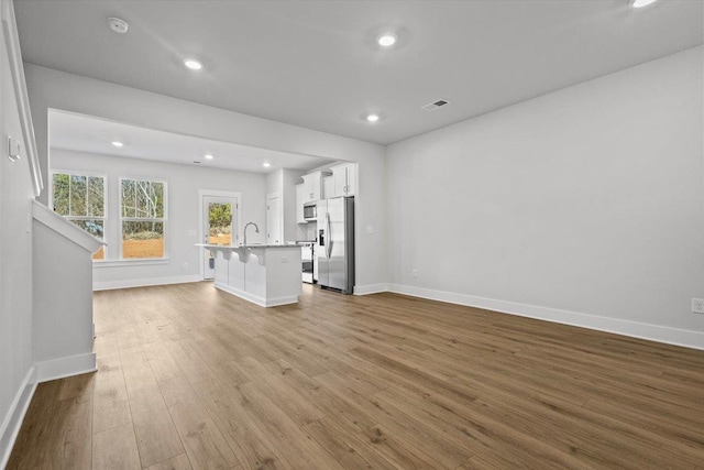 unfurnished living room with sink and light hardwood / wood-style floors