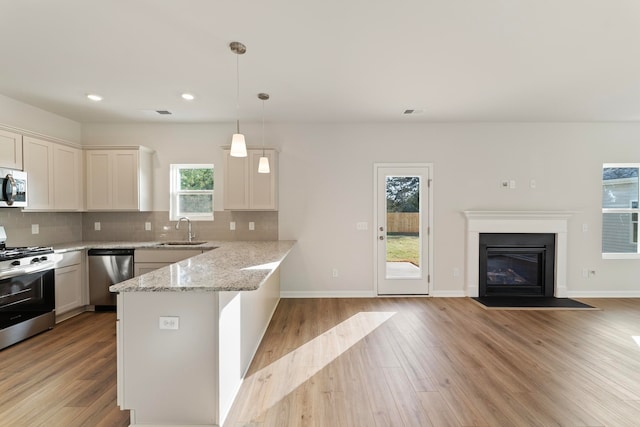 kitchen with sink, light wood-type flooring, decorative light fixtures, kitchen peninsula, and stainless steel appliances