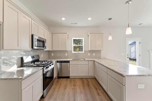 kitchen featuring sink, stainless steel appliances, kitchen peninsula, light hardwood / wood-style floors, and decorative light fixtures