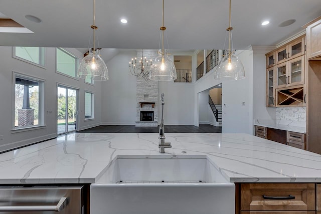 kitchen with pendant lighting, an inviting chandelier, a stone fireplace, sink, and light stone countertops