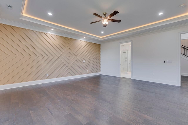 unfurnished room featuring ceiling fan, a raised ceiling, dark hardwood / wood-style flooring, wood walls, and crown molding