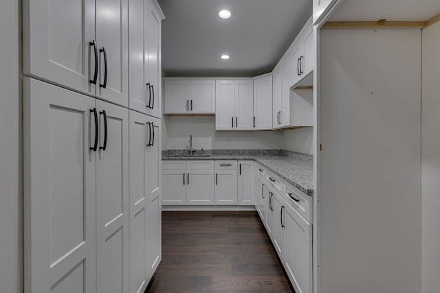 kitchen with white cabinets, dark hardwood / wood-style floors, light stone countertops, and sink