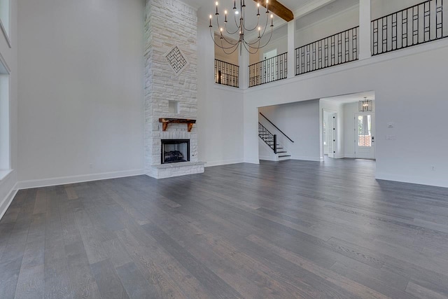 unfurnished living room featuring a high ceiling, dark hardwood / wood-style floors, a stone fireplace, and a notable chandelier