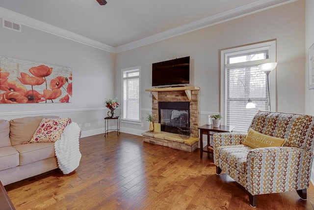 living room featuring a stone fireplace, wood-type flooring, and crown molding