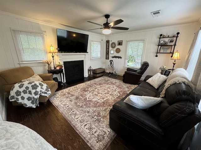 living area featuring hardwood / wood-style flooring, a fireplace with flush hearth, visible vents, and ornamental molding