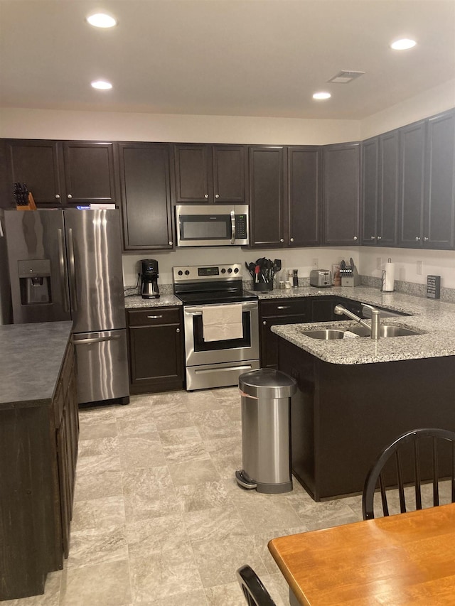 kitchen with light stone countertops, appliances with stainless steel finishes, dark brown cabinets, and sink