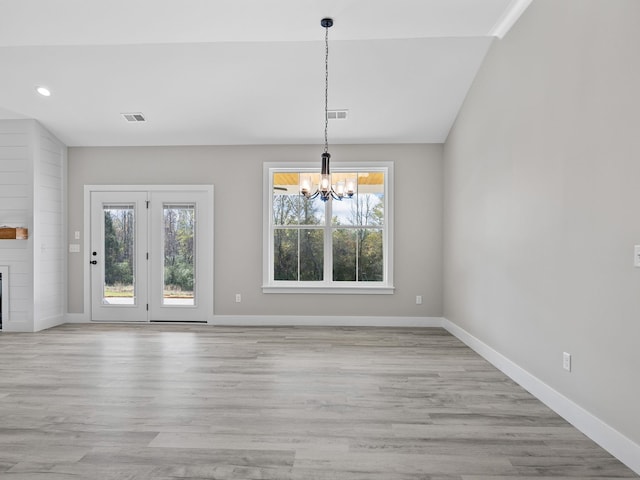 unfurnished dining area featuring a fireplace, a chandelier, vaulted ceiling, and light wood-type flooring