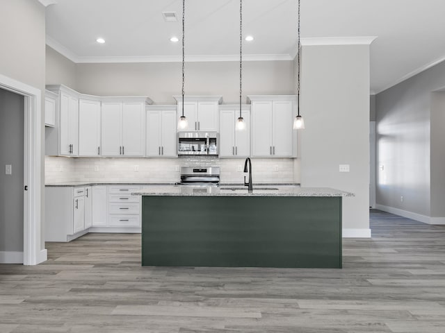 kitchen with light stone countertops, white cabinetry, stainless steel appliances, a center island with sink, and light wood-type flooring