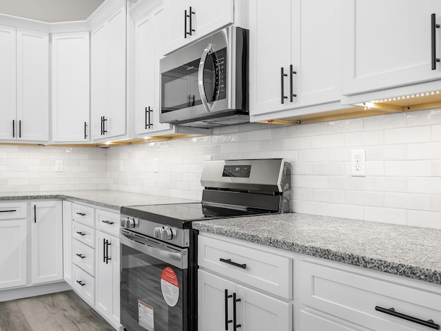 kitchen featuring light stone countertops, decorative backsplash, stainless steel appliances, light hardwood / wood-style floors, and white cabinetry