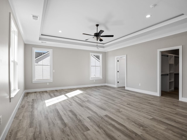 empty room with a raised ceiling, a wealth of natural light, and light wood-type flooring