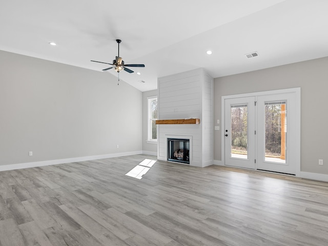 unfurnished living room featuring lofted ceiling, a large fireplace, light wood-type flooring, and ceiling fan