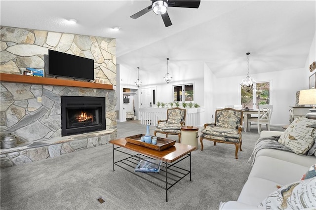 carpeted living room featuring ceiling fan with notable chandelier, a stone fireplace, and vaulted ceiling