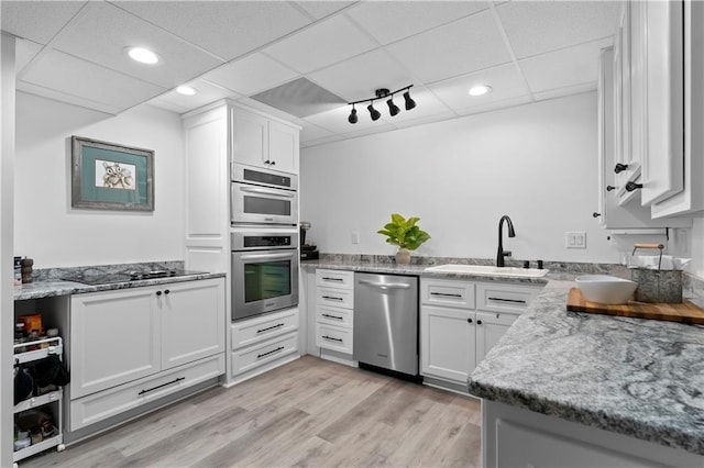 kitchen featuring appliances with stainless steel finishes, white cabinetry, a drop ceiling, and sink