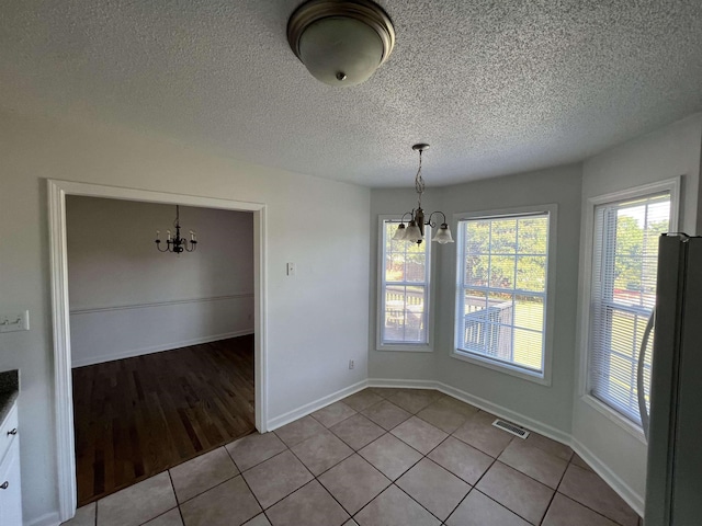 unfurnished dining area featuring light tile patterned floors, a textured ceiling, and an inviting chandelier