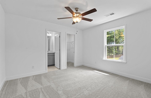 unfurnished bedroom featuring light carpet, ceiling fan, ensuite bath, a closet, and a walk in closet