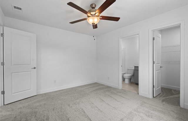 unfurnished bedroom with ensuite bathroom, ceiling fan, a closet, light colored carpet, and a walk in closet