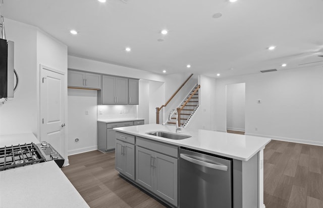 kitchen featuring stainless steel appliances, sink, dark hardwood / wood-style floors, gray cabinets, and a kitchen island with sink