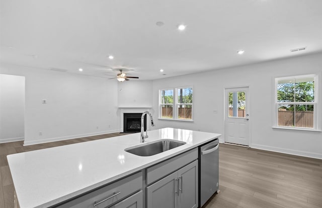 kitchen featuring hardwood / wood-style floors, an island with sink, gray cabinetry, dishwasher, and sink