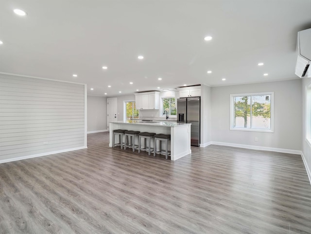 kitchen with white cabinetry, stainless steel refrigerator with ice dispenser, a breakfast bar, a kitchen island, and light wood-type flooring