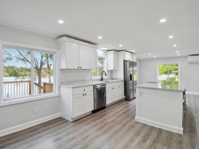 kitchen with white cabinetry, sink, stainless steel appliances, a wall mounted AC, and light wood-type flooring