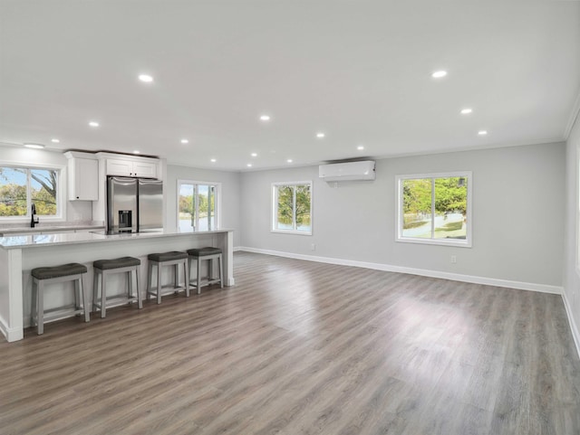 unfurnished living room with a wall mounted air conditioner, hardwood / wood-style floors, and a wealth of natural light