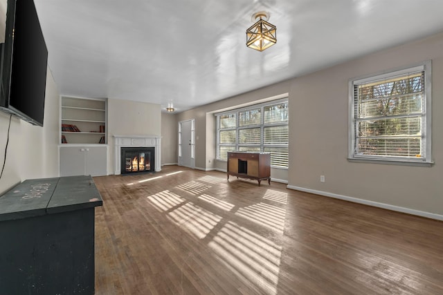 unfurnished living room featuring built in features, a fireplace, baseboards, and wood finished floors