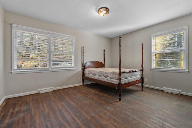 bedroom featuring a baseboard heating unit, wood finished floors, visible vents, and baseboards