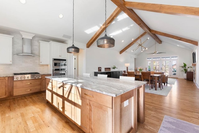 kitchen with a kitchen island, wall chimney range hood, white cabinetry, and appliances with stainless steel finishes