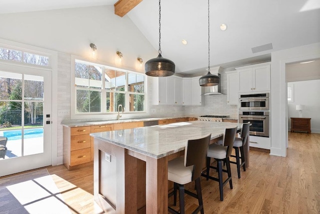 kitchen featuring light wood-type flooring, light stone counters, a center island, white cabinetry, and hanging light fixtures