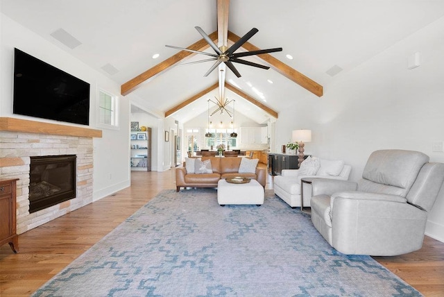 living room with vaulted ceiling with beams, light hardwood / wood-style floors, a fireplace, and ceiling fan with notable chandelier