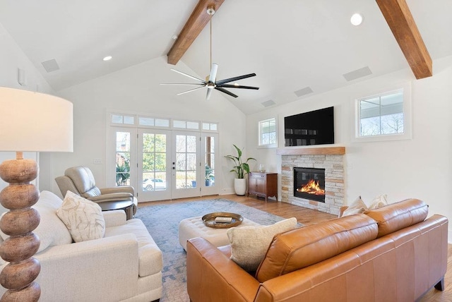 living room featuring french doors, light wood-type flooring, ceiling fan, beamed ceiling, and a stone fireplace