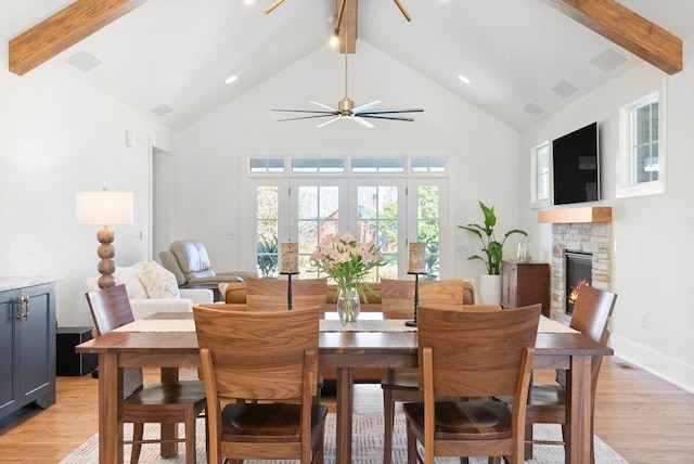 dining space featuring ceiling fan, beam ceiling, high vaulted ceiling, light hardwood / wood-style flooring, and a fireplace