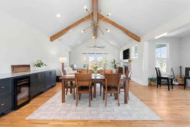 dining area with lofted ceiling with beams, ceiling fan with notable chandelier, wine cooler, a fireplace, and light hardwood / wood-style floors