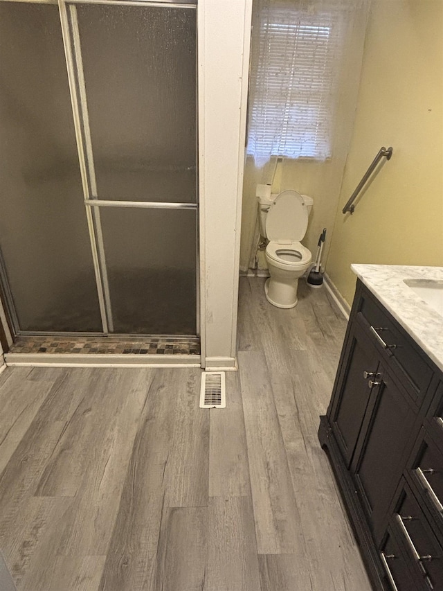 bathroom featuring vanity, wood-type flooring, toilet, and walk in shower