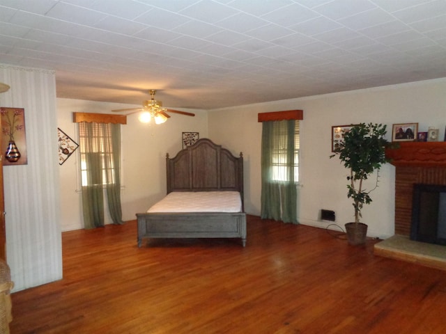 bedroom featuring a fireplace, dark hardwood / wood-style flooring, and ceiling fan