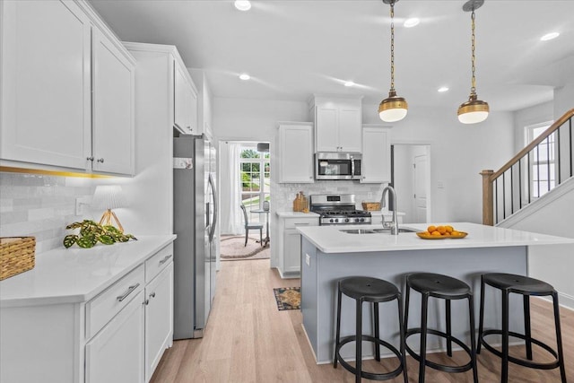 kitchen with white cabinets, sink, hanging light fixtures, light hardwood / wood-style flooring, and stainless steel appliances