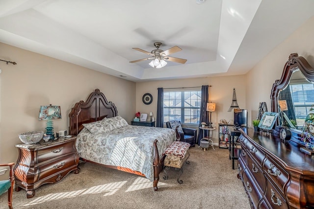 carpeted bedroom with ceiling fan and a tray ceiling