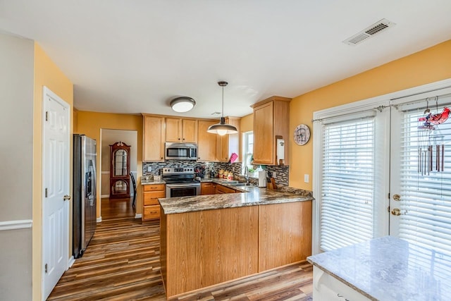 kitchen featuring kitchen peninsula, pendant lighting, stainless steel appliances, and plenty of natural light