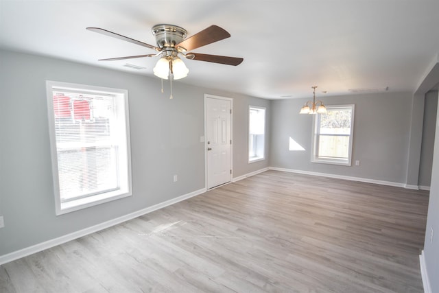 empty room featuring ceiling fan with notable chandelier and light wood-type flooring