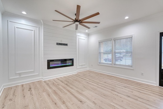 unfurnished living room featuring light wood-type flooring, a large fireplace, ceiling fan, and crown molding