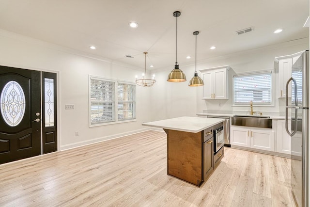 kitchen with a center island, sink, light hardwood / wood-style flooring, pendant lighting, and white cabinets