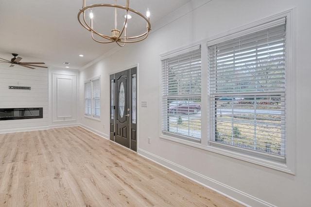 foyer entrance featuring a fireplace, ornamental molding, ceiling fan with notable chandelier, and light wood-type flooring