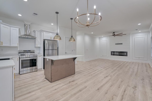 kitchen with stainless steel appliances, wall chimney range hood, decorative light fixtures, light hardwood / wood-style floors, and white cabinetry