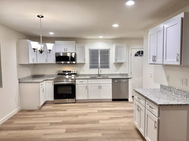 kitchen featuring white cabinets, sink, appliances with stainless steel finishes, light hardwood / wood-style floors, and light stone counters