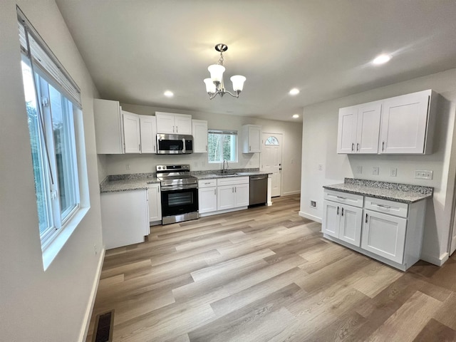 kitchen with light wood-type flooring, stainless steel appliances, a notable chandelier, white cabinets, and hanging light fixtures