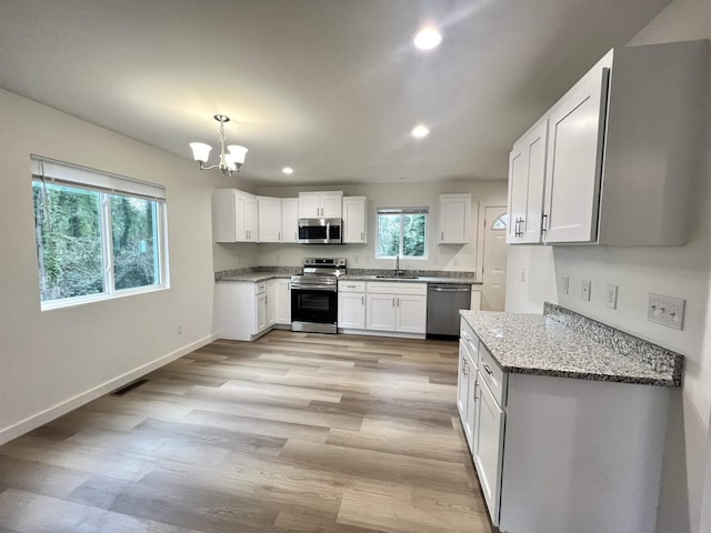 kitchen with white cabinets, hanging light fixtures, light hardwood / wood-style flooring, light stone countertops, and appliances with stainless steel finishes