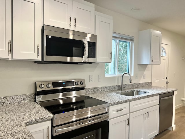 kitchen with light stone counters, stainless steel appliances, sink, light hardwood / wood-style flooring, and white cabinetry