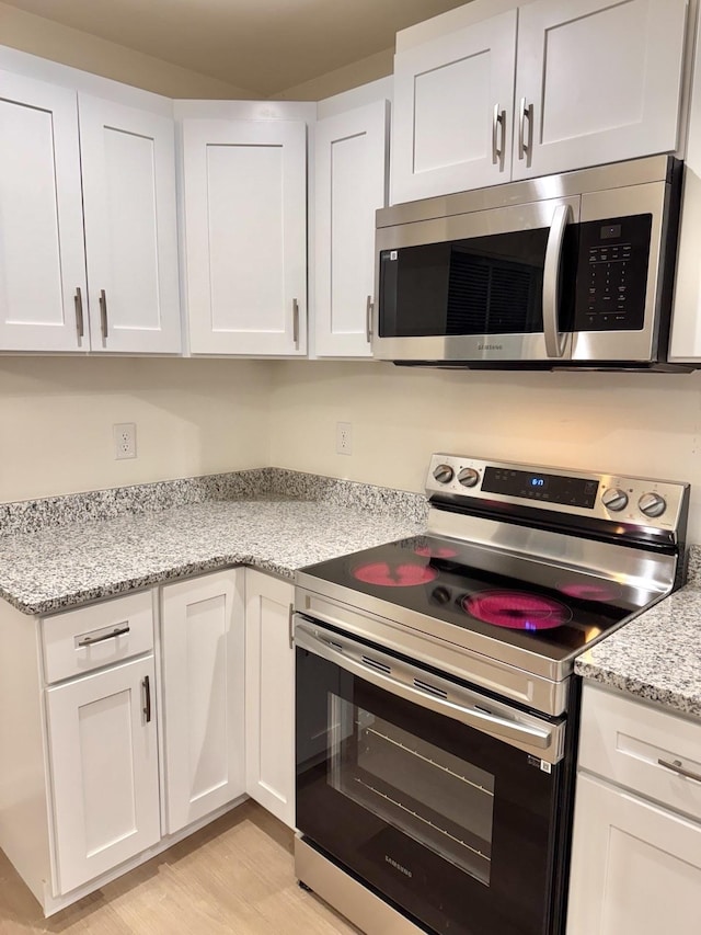 kitchen featuring white cabinetry, light hardwood / wood-style flooring, stainless steel appliances, and light stone counters