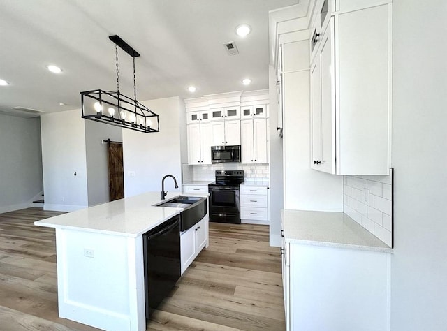 kitchen with black appliances, white cabinets, light wood-type flooring, and an island with sink